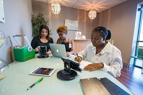 Three females working on various personal devices around one table